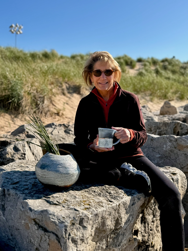 cyndi Casemier holding her handmade ceramic mug and vase. She uses lake michigan beach sand in her exterior glaze for one of a kind pottery.