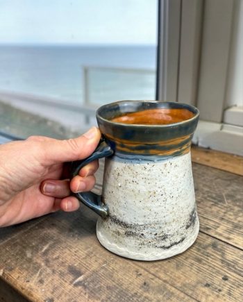 Lake Michigan ceramic mug held in hand showing scale, textured handle, and layered shoreline glaze