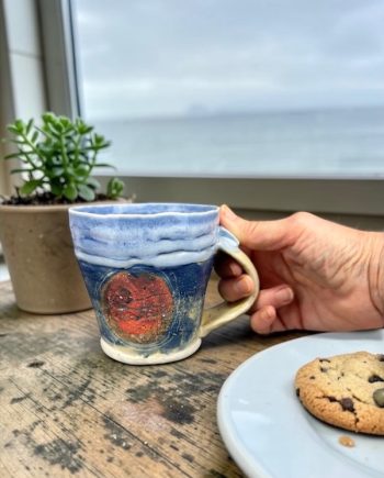 Lake Michigan ceramic mug with sun motif on countertop, showing layered blue glaze and form